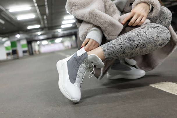 leather sneakers white gray demi season. On foot, a model in an underground parking lot. Sheepskin coat. Snake skin print leggings - Foto, Bild