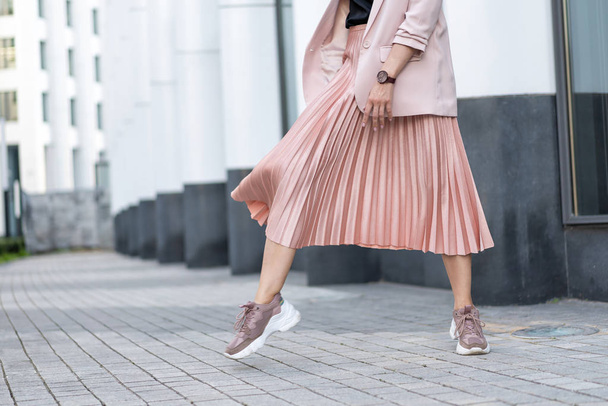 Pleated skirt coral color and sneakers. The girl is very dynamic posing on the street, the skirt is developing. - Photo, image