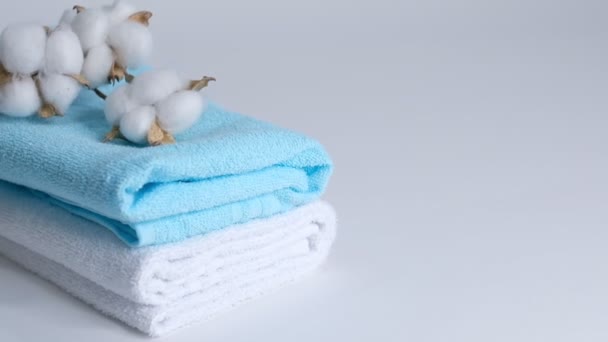 asciugamani puliti bianchi e blu e un ramo di cotone su sfondo bianco. Primo piano rallentatore
. - Filmati, video