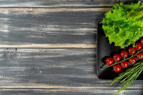 branch cherry tomatoes and lettuce on black plate on wooden table. copy space - Foto, imagen