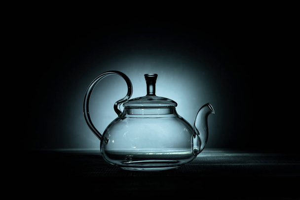 empty glass teapot on black background in spot light, copy space - Valokuva, kuva