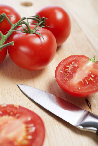 Fresh tomatoes being sliced on a wooden chopping board with knife - Фото, зображення