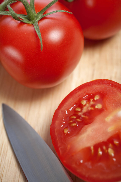 Fresh tomatoes being sliced on a wooden chopping board with knife - Foto, afbeelding