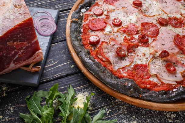 Pizza à partir d'une pâte noire non conventionnelle avec jambon, saucisse et sauce tomate
 - Photo, image