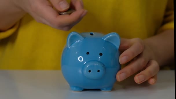 Piggy Bank iş konsepti. Bir el, mavi arka plandaki kumbaraya para koyuyor. Para biriktirmek gelecek için bir yatırımdır. Banka yatırımı. - Video, Çekim
