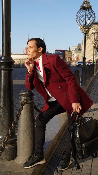 attractive man in red coat posing in full length while walking in center of Moscow at sunny day - Φωτογραφία, εικόνα