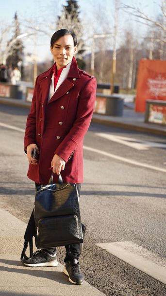 attractive man in red coat posing in full length while walking in center of Moscow at sunny day - Foto, Imagen