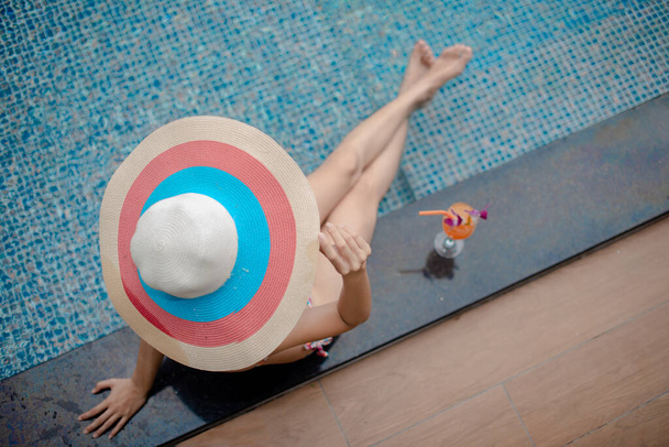 młoda kobieta trzyma kapelusz cieszyć się latem w basenie, pomarańczowy odświeżyć wzdłuż picia - Zdjęcie, obraz