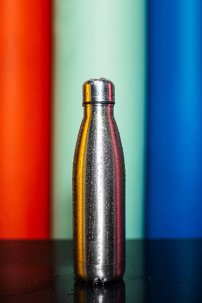 Gros plan de la bouteille thermo en acier réutilisable pulvérisée avec de l'eau sur fond de lave luxuriante, aqua menthe et bleu fantôme de couleur
. - Photo, image