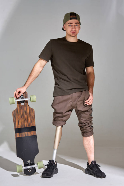 Disabled young man with leg prosthesis with longboard skateboard on white background. Sun light. - Foto, Bild
