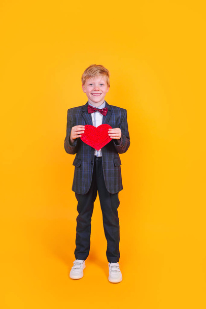 Happy smiling handsome boy with a red heart on yellow background. Valentines Day - Foto, immagini