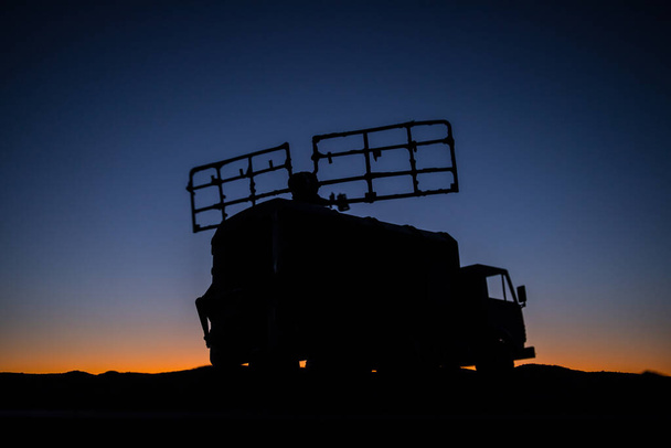 Kreative Dekoration der Kunstwerke. Silhouette eines mobilen Luftverteidigungsfahrzeugs mit Radarantenne während des Sonnenuntergangs. Satellitenschüsseln oder Radioantennen gegen den Abendhimmel. Selektiver Fokus - Foto, Bild