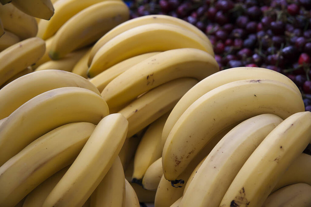 Ripe banana bunches placed on cherries on a market counter - Φωτογραφία, εικόνα