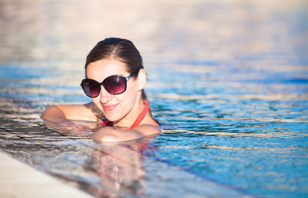 Portrait of a young woman relaxing in a swimming pool (shallow DOF - Foto, immagini