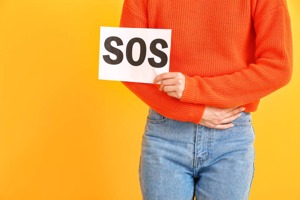 Young woman holding paper with text SOS on color background. Menstruation concept - Photo, Image