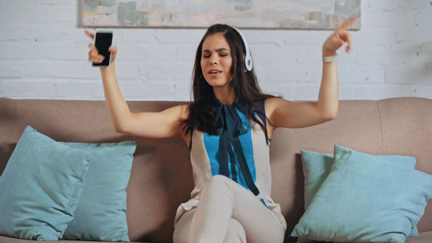 šťastná žena v bezdrátových sluchátkách držící smartphone  - Záběry, video
