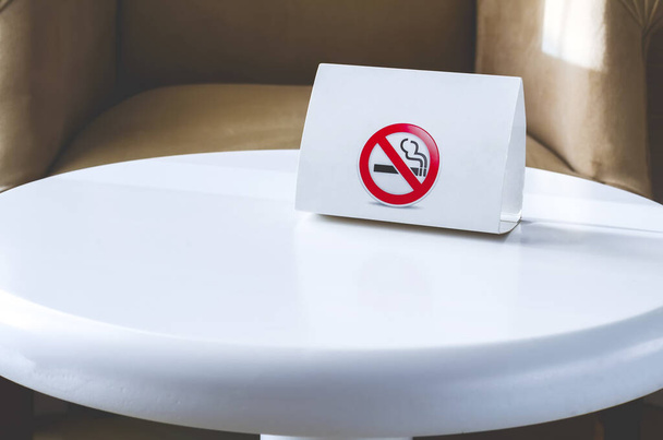 Valkoinen pahvi merkki Ei tupakointia valkoisella pyöreällä pöydällä. Hotellin sisustus
 - Valokuva, kuva