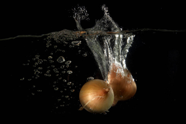 Onions dropped into water in front of a black background - Φωτογραφία, εικόνα
