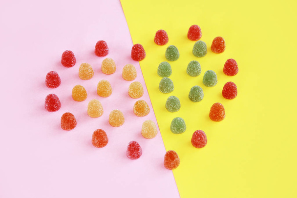 corazón hecho de dulces dulces de mermelada redonda multicolor con salpicaduras de azúcar sobre un fondo rosa amarillo
 - Foto, Imagen