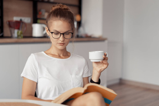Χαριτωμένο κορίτσι πίνει καφέ και διαβάζει ένα βιβλίο. - Φωτογραφία, εικόνα