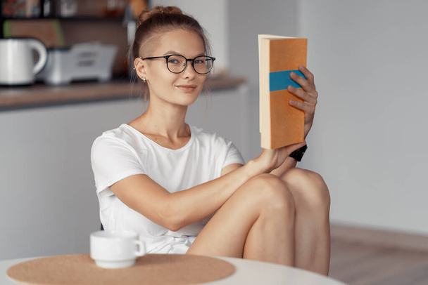 Cute girl is drinking coffee and reading a book - Zdjęcie, obraz
