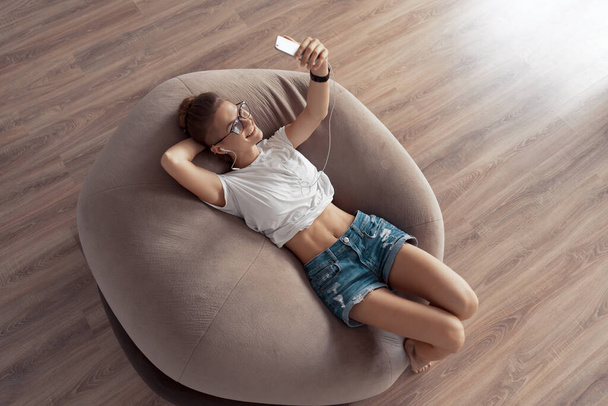 Young girl is lying on a chair bag and listening to music from your phone - Fotoğraf, Görsel