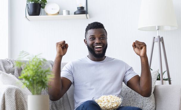 Emocionado hombre afroamericano disfrutando de los deportes en la televisión en casa
 - Foto, imagen