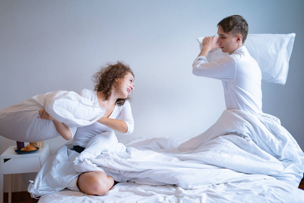 Young couple in pajamas having fun together in bed, having pillow fight - Foto, Bild