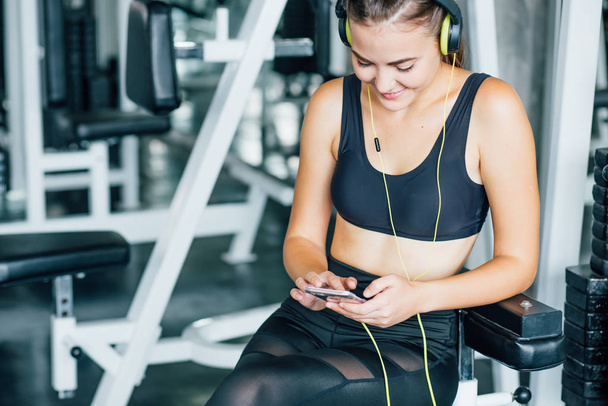 Active girl using smartphone in fitness gym. Young woman workout in gym healthy lifestyle. Young woman using phone in gym. Change for health concept. - Photo, image