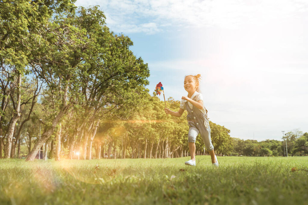 Дівчина грає і біжить навколо парку в красивий ранок, дочка насолоджується сонячним садовим відпочинком, простором на відкритому повітрі, способом дозвілля, щасливим викладанням з полум'ям світлого неба в парку
. - Фото, зображення