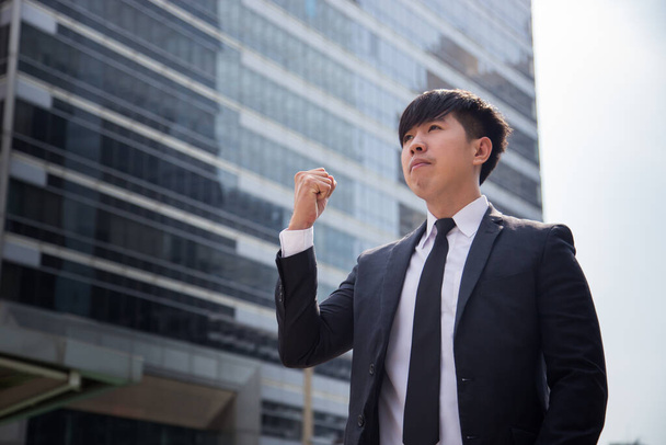 Modern ázsiai üzletember. Magabiztos fiatalember teljes öltönyben, elfordítja a tekintetét, miközben a szabadban áll, a háttérben városképpel.. - Fotó, kép
