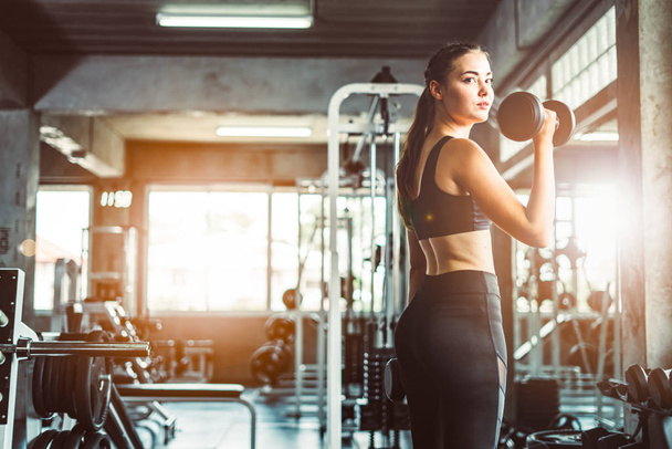 Young girl playing dumbbell to exercise in fitness.Slim girl lifts heavy dumbbell while training in the gym. Sports concept fat burning and a healthy lifestyle. - Photo, Image