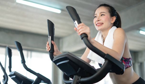 Fit Asian woman exercising on bicycle in fitness center. - Foto, imagen
