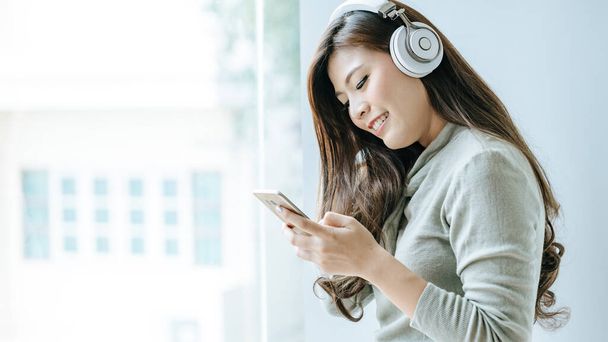 Beautiful girl is working on smartphone and listening to music by headphone.Office girls relax by listening to music. - 写真・画像