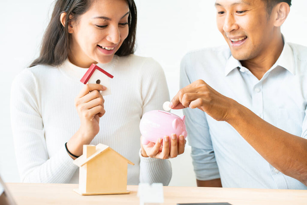 woman putting a coin into a pink piggy bank concept for savings and finance.The best choice of house.House owner and architect discussing a choice.Couple dreaming of new home. - Photo, image