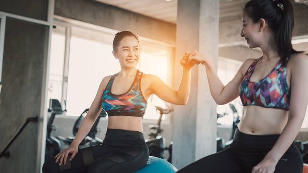 Beautiful Asian women giving fist-bump while working out in gym together. - Foto, Bild