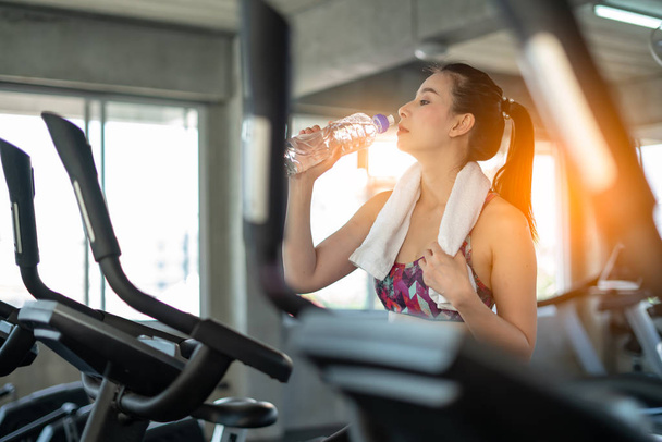 Gym woman drinking water on bicycle in sport club - Zdjęcie, obraz