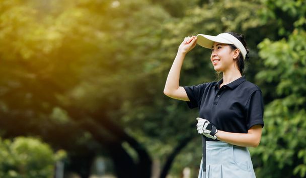 Asian female golfer look happy with her golf game.Professional female golfer holding golf club on field and looking away. - Photo, image