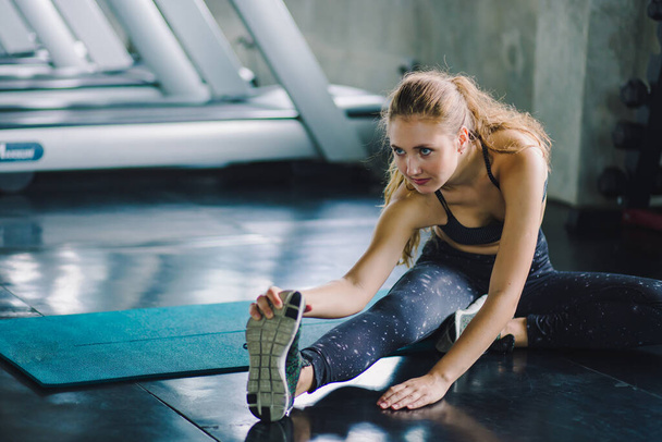 Vrouw in de sportschool doet stretching oefeningen en glimlacht op de vloer.Sportieve achtergrond. - Foto, afbeelding