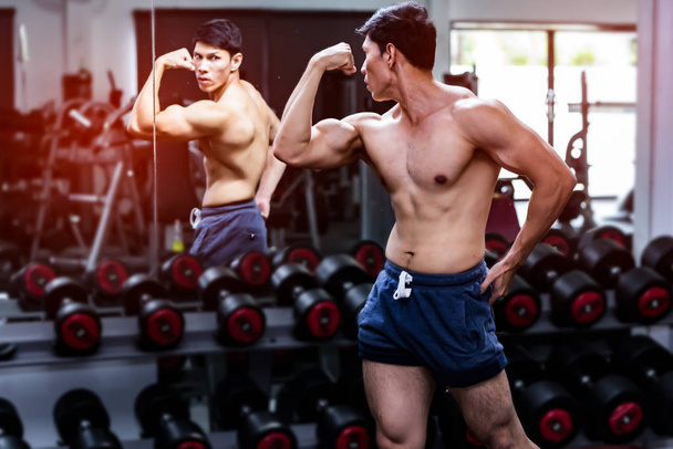 Muscular man posing in front of mirror in gym, concept for body health. - Photo, Image