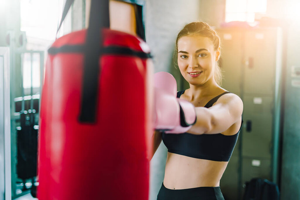Portrait of a confident young athlete woman posing in boxing gloves.Attractive Female Punching A Bag With Boxing Gloves On. - Photo, Image