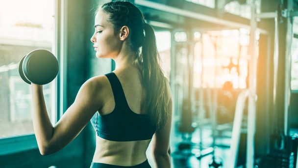 Young girl playing dumbbell to exercise in fitness.Slim girl lifts heavy dumbbell while training in the gym. Sports concept fat burning and a healthy lifestyle. - Foto, Imagem