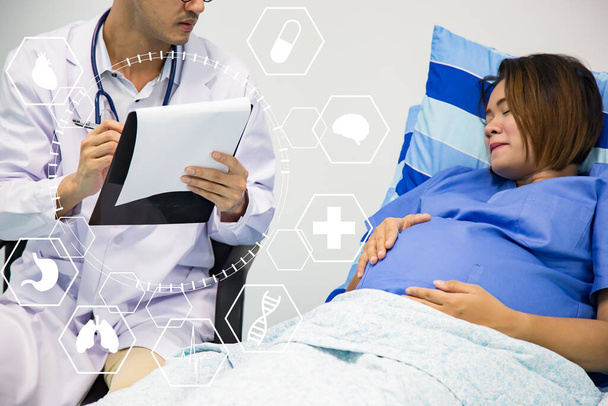 Kobieta w ciąży otrzymuje Ante Natal sprawdzić przez lekarza gospodarstwa schowka patrząc na notatki.Asian lekarz konsulting z ciężarnej azjatyckiej kobiety. - Zdjęcie, obraz