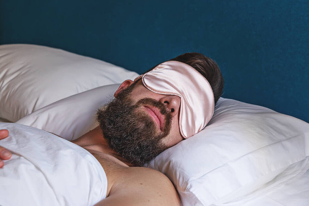 Καυκάσιος γενειοφόρος άνδρας στο eyemask κοιμάται στο κρεβάτι - Φωτογραφία, εικόνα