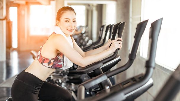 Fit Asian woman exercising on bicycle in fitness center. - Foto, Bild