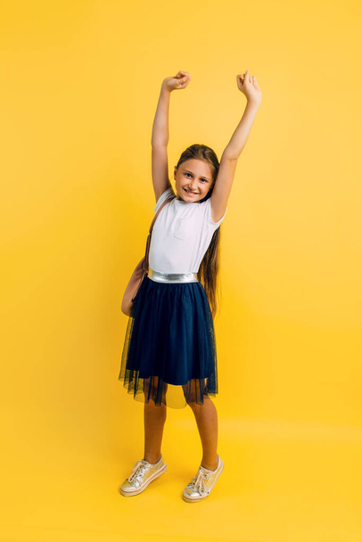 Charming little student on a yellow background. The pupil of a small child adores school. Emotional schoolgirl - Foto, afbeelding
