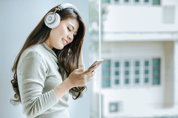 Beautiful girl is working on smartphone and listening to music by headphone.Office girls relax by listening to music. - Photo, Image