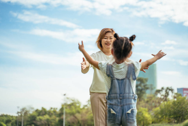 Nice little girl run to grandmother's hug in park.Grandmother and grand daughter enjoying sunny garden holiday together, outdoors space, leisure lifestyle,happy teaching with flare light sky in park. - Photo, Image