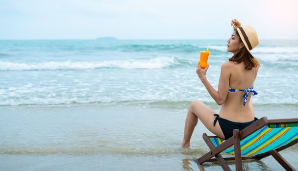 Happy woman in bikini relaxing in chair on beach with tropical cocktail. - Фото, зображення