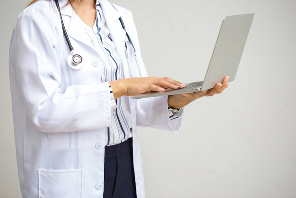 Lékař pracující s notebookem. Žena lékař se stetoskopem pracuje s počítačem na bílém pozadí. - Fotografie, Obrázek